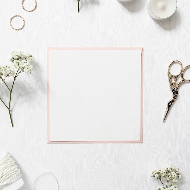 Blank white paper surrounded with rings; gypsophila; string; candles and scissor on white background