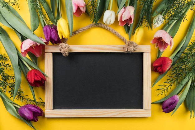 Blank wooden slate decorated with colorful fresh tulips against yellow background