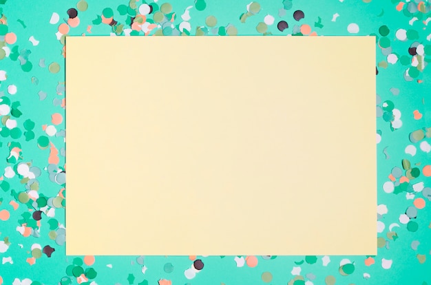 Blank yellow paper with colorful confetti over green background