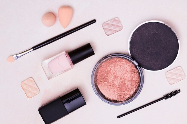 Blender sponge; makeup brush; eyeshadow; compact face powder on pink background