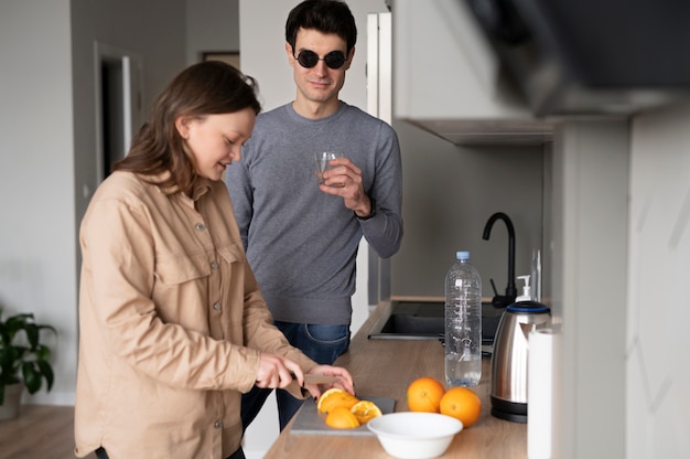 Blind man drinking a glass of water while a woman is slicing an orange Free Photo