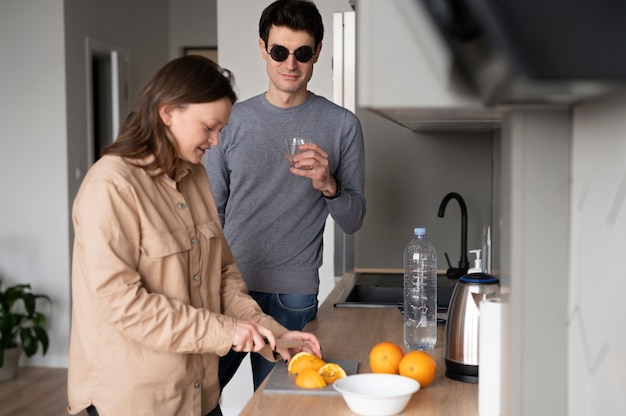 Blind man drinking a glass of water while a woman is slicing an orange