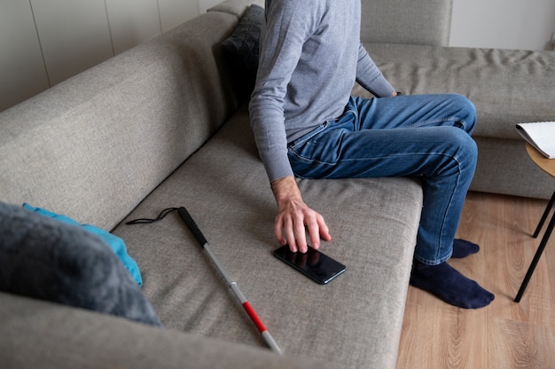 Free photo blind man taking his smartphone from the couch