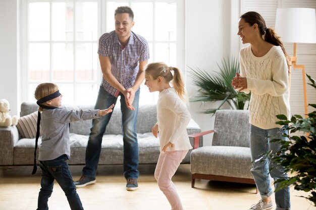 Blindfolded cute boy playing hide and seek game with family