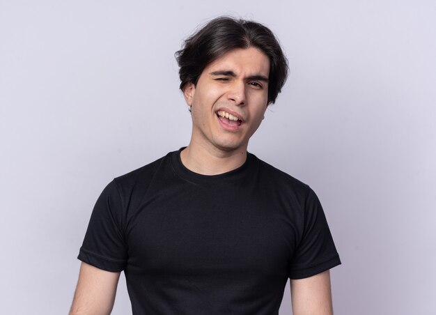 Blinked looking at front young handsome guy wearing black t-shirt isolated on white wall