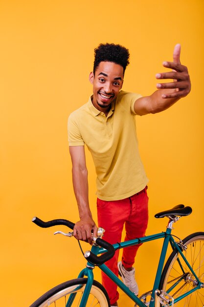 緑の自転車でポーズをとる至福のアフリカ人。自転車で立っている感情的なブルネットの男性モデルの屋内ショット。