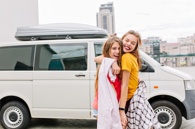 Blissful brown-haired girl with happy smile embracing her best friend with trendy hairstyle