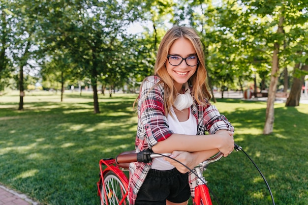 笑顔で見ている自転車と至福のかわいい女性。春の週末を楽しんでいるゴージャスな白人の女の子の屋外ショット。