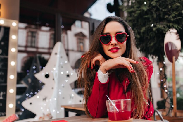 Blissful girl with stylish manicure sitting in outdoor cafe with modern exterior