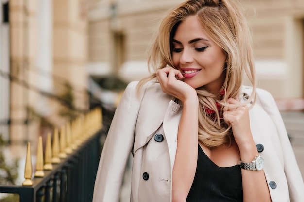 Blissful lightly-tanned european lady wears stylish jacket having fun after work day and laughing. Close-up outdoor photo of charming female model with elegant hairstyle enjoying good morning.