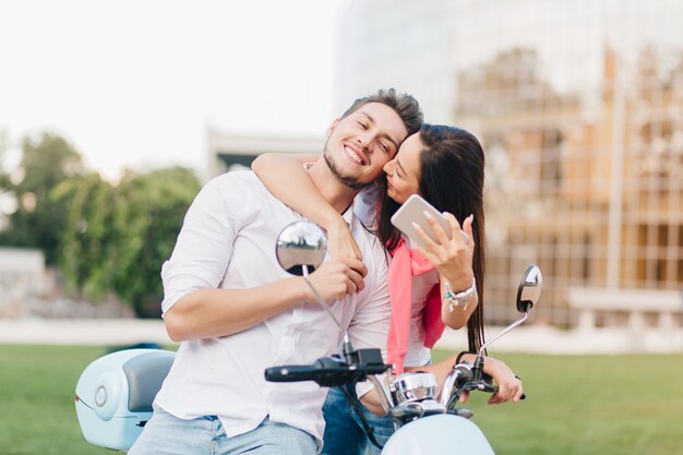 Blissful man posing on scooter while his friend kissing him