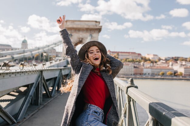 Blissful pale woman in coat expressing true emotions while posing on bridge in warm day