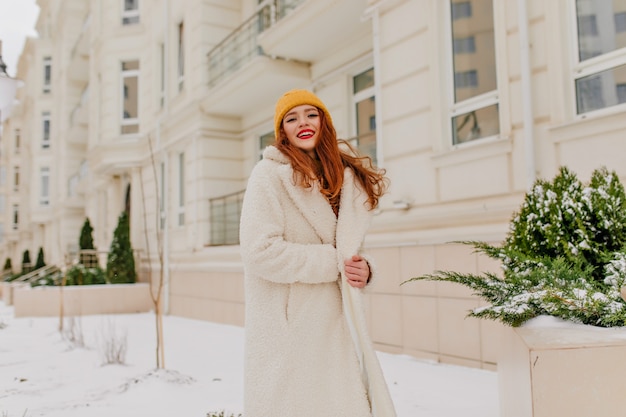 Foto gratuita beata donna in cappotto lungo in posa a dicembre. ritratto di inverno della ragazza dello zenzero con un sorriso allegro.