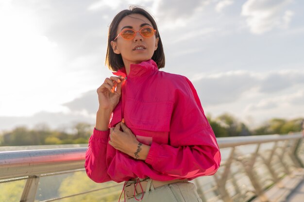 Blissful woman in stylish sportive pink jacket walking early morning