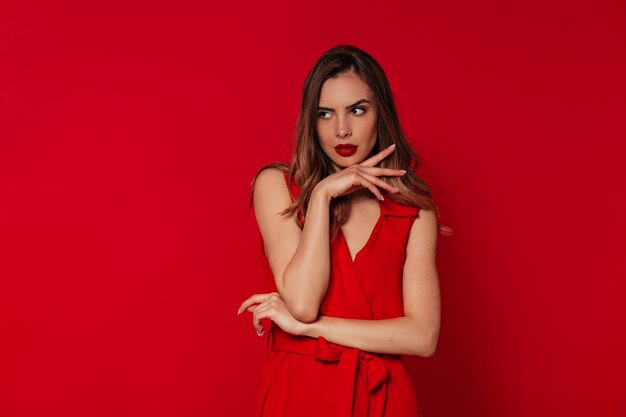 Blissful woman with evening make up wearing red dress posing over red wall