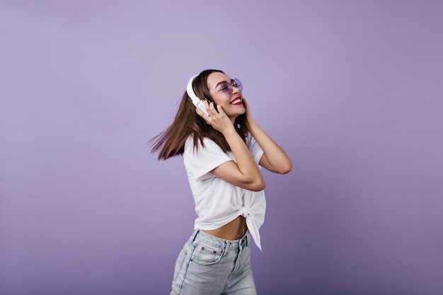 Blissful young woman in casual white t-shirt dancing. Ecstatic caucasian girl in trendy clothes relaxing with headphones.