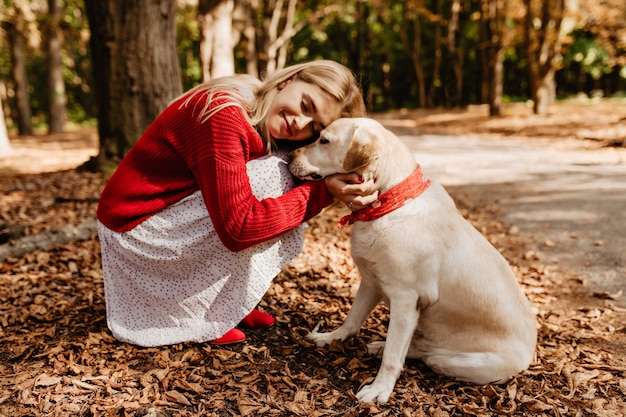 Blissfully happy blonde girl smiling close to her dog. Beautiful woman feeling happy with beloved pet.