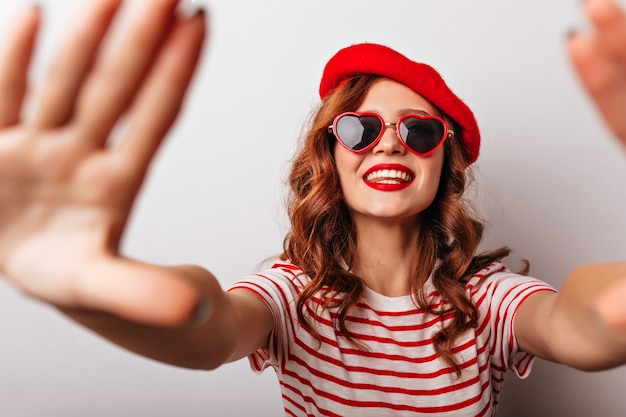 Blithesome caucasian girl in red beret having fun . Enchanting ginger female model posing in sunglasses.