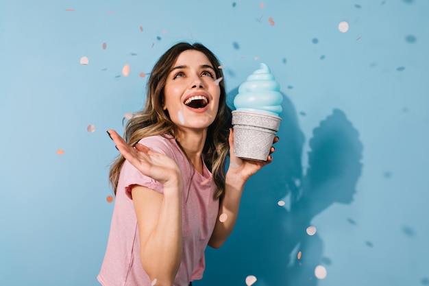 Blithesome darkhaired woman posing with ice cream carefree girl smiling on blue background