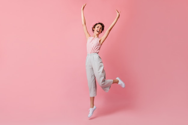 Blithesome french woman in pants jumping with hands up