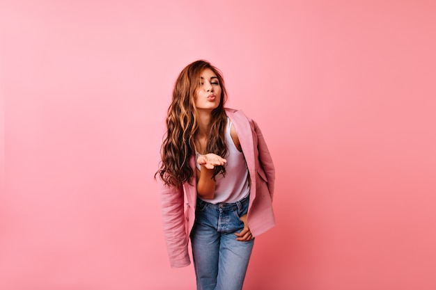 Blithesome girl in jeans posing with kissing face expression. Appealing red-haired lady sending air kiss.