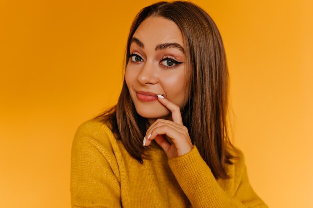 Blithesome tanned woman posing with interested smile. Indoor photo of adorable girl in trendy yellow sweater.