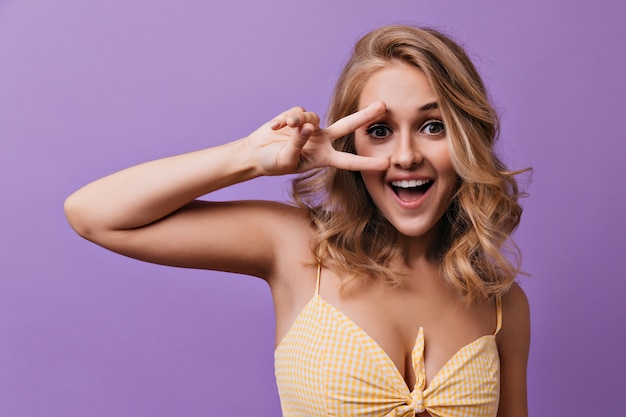 Blithesome woman with romantic wavy hairstyle posing with peace sign. Lovely elegant girl fooling around.