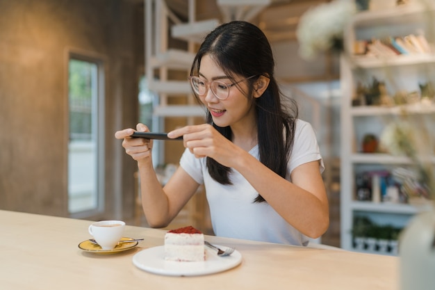 ブロガーアジア人フレンドリーな女性インフルエンサーがナイトカフェでケーキを食べる