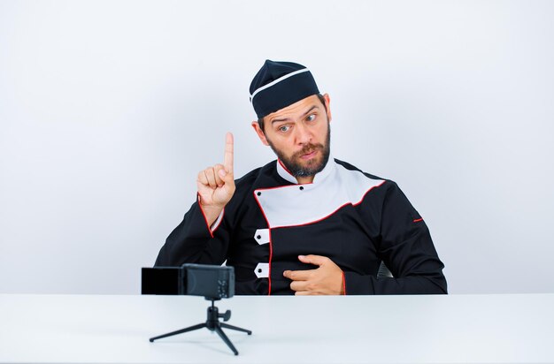 Blogger chef is showing a minute gesture by sitting in front of his mini camera on white background