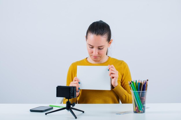 Blogger girl is holding white paper and looking down on white background