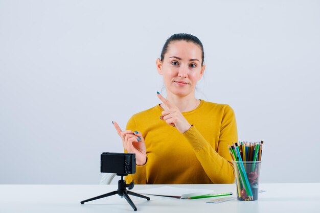 Blogger girl is pointing left with forefingers by sitting on white background