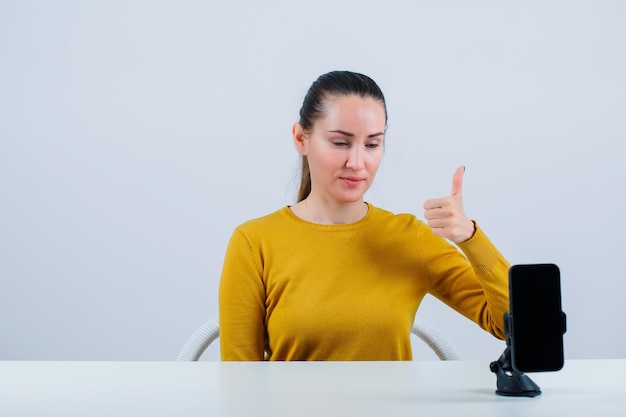 Blogger girl is posing by showing perfect gesture in front of mobile camera on white background