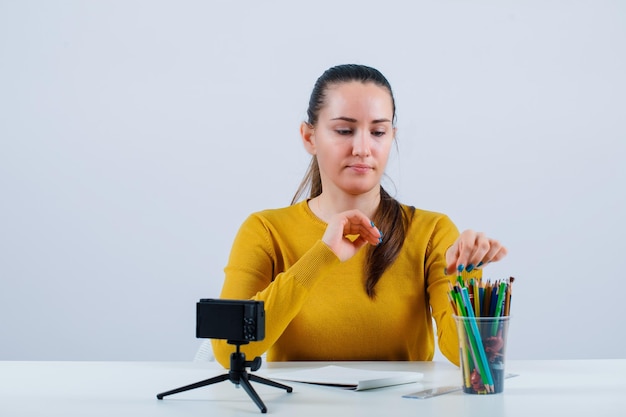 Blogger girl is taking a pencil from pencil case on white background