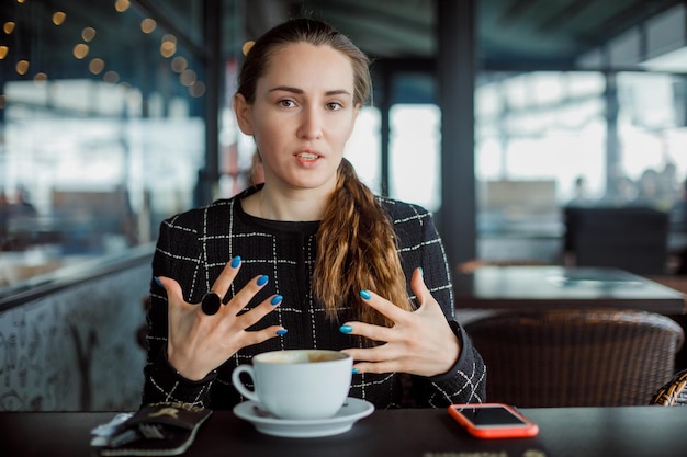 Blogger girl is talking by opening wide her hands in cafe