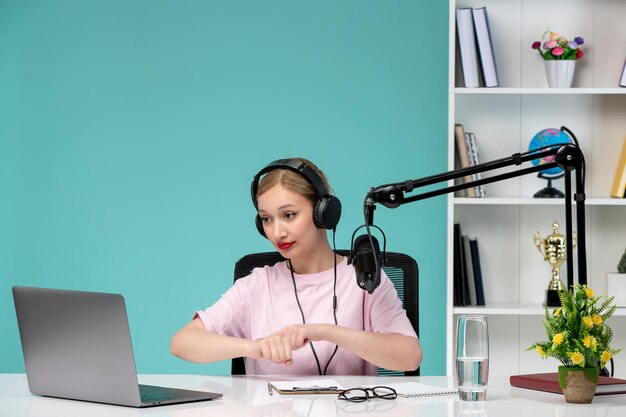 Blogger journalist young cute blonde girl recording video on computer in office showing at clocks