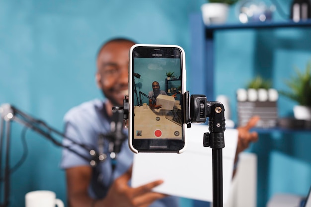 Blogger making giveaway while live streaming on smartphone screen closeup. Web content creator announcing contest and showing prize gift using mobile phone on tripod for video recording