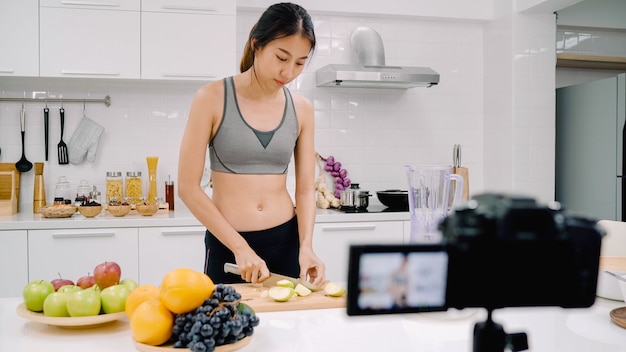 彼女の加入者のためにリンゴジュースのビデオを作る方法を記録するカメラを使用しているブロガーのスポーティーなアジアの女性