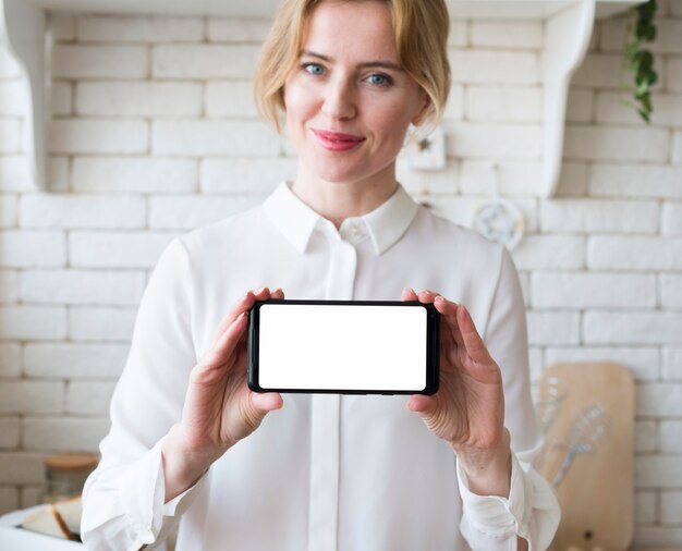 空白の画面を持つスマートフォンを保持している金髪のビジネス女性