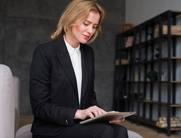 Блондинка деловая женщина сидит и с помощью планшета