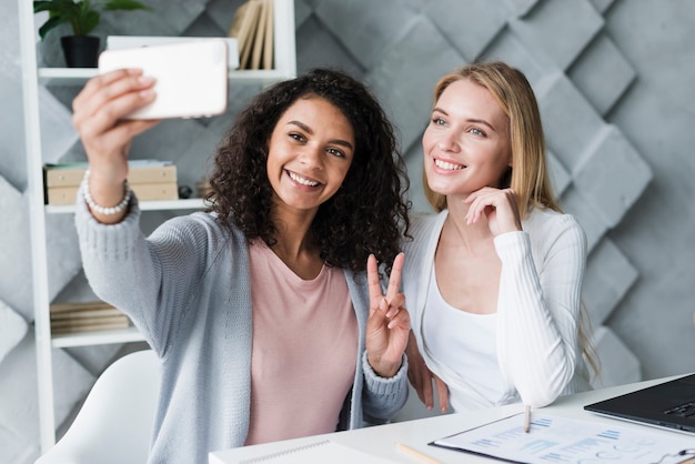 Free photo blond and ethnic coworkers doing selfie at workplace