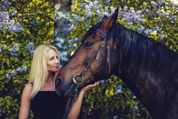 茶色の馬とポーズをとって黒いイブニングドレスの金髪の女性。