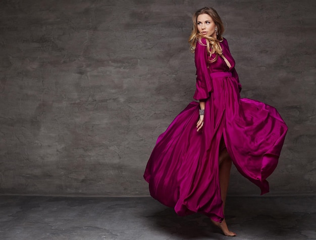 Blond female in long red dress in motion. Studio shoot.