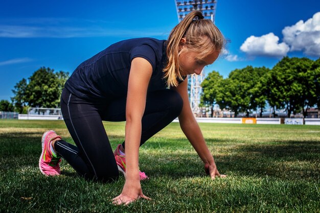 Blond female in sportswear doing exercises on the stadium.