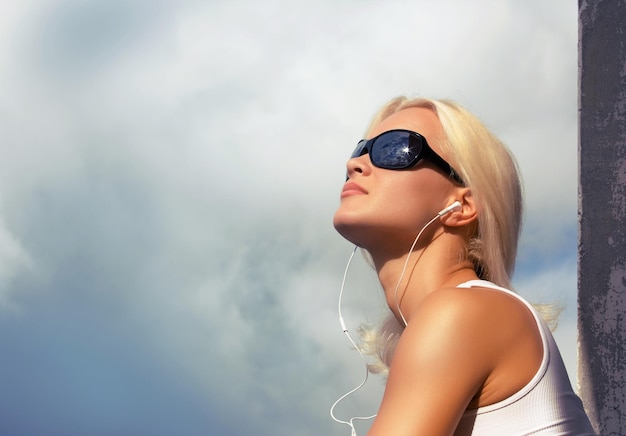 Blond female in sunglasses listening music. outdoor shot