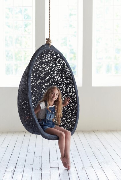 Blond female teenager relaxing in round black artistic chair.