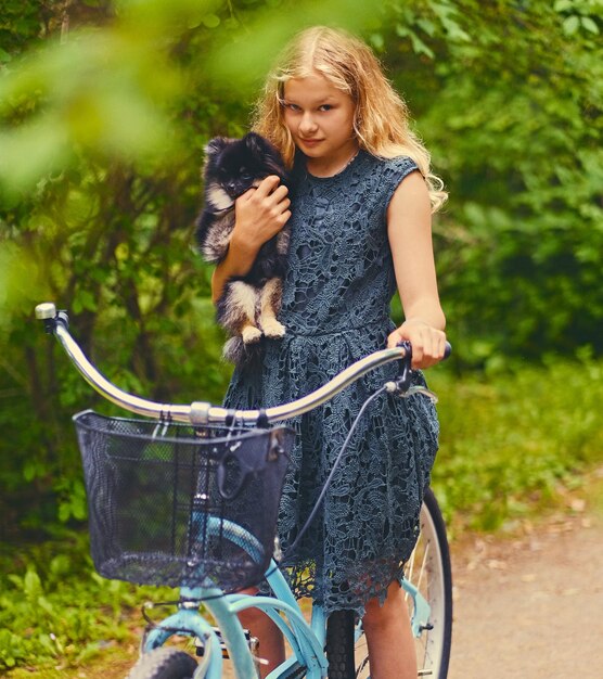 自転車に乗ったブロンドの女の子がスピッツ犬を抱いています。