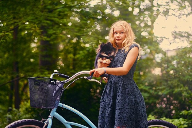 자전거를 탄 금발 소녀가 스피츠 개를 안고 있습니다.