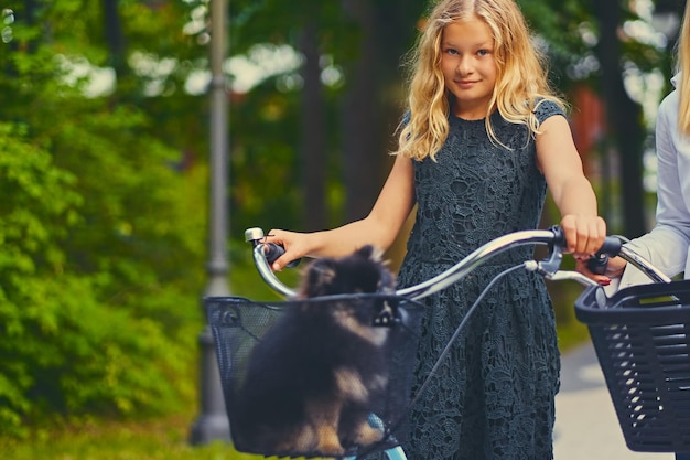 Free photo blond girl on a bicycle and a spitz dog in a basket.