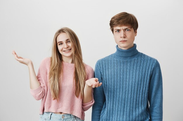 Blond girl smiling and shrugging while guy feel frustrated or confused, frowning angry.