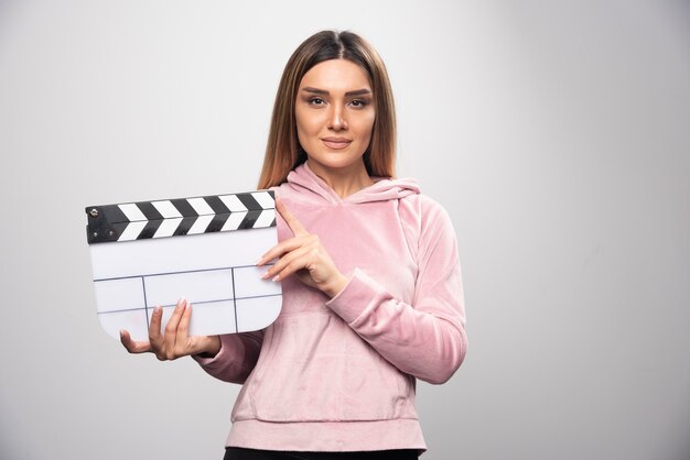 Blond lady in pink sweatshier holding a blank clapper board and gives natural poses.